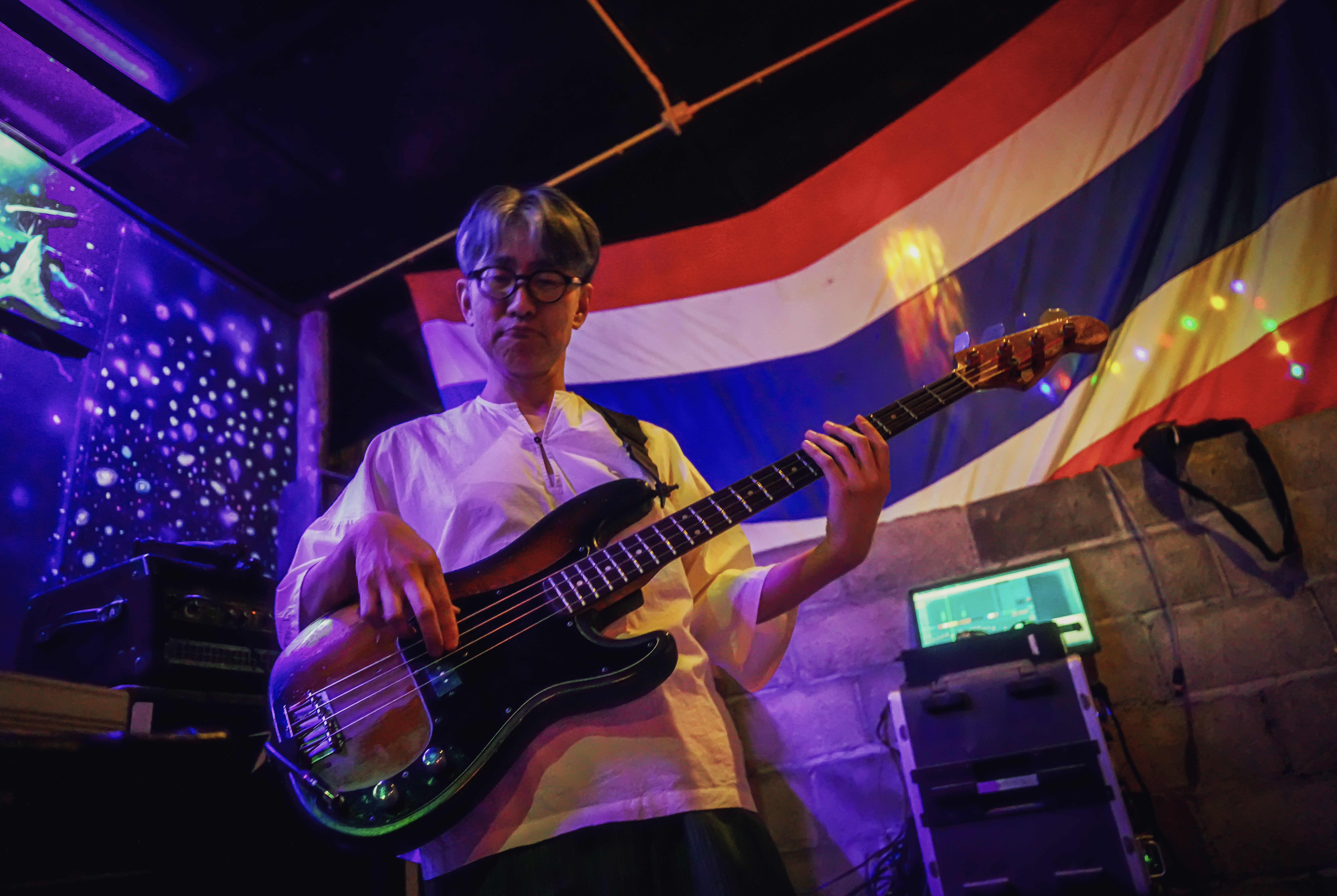 Guitarist performing on stage with Thai flag backdrop.