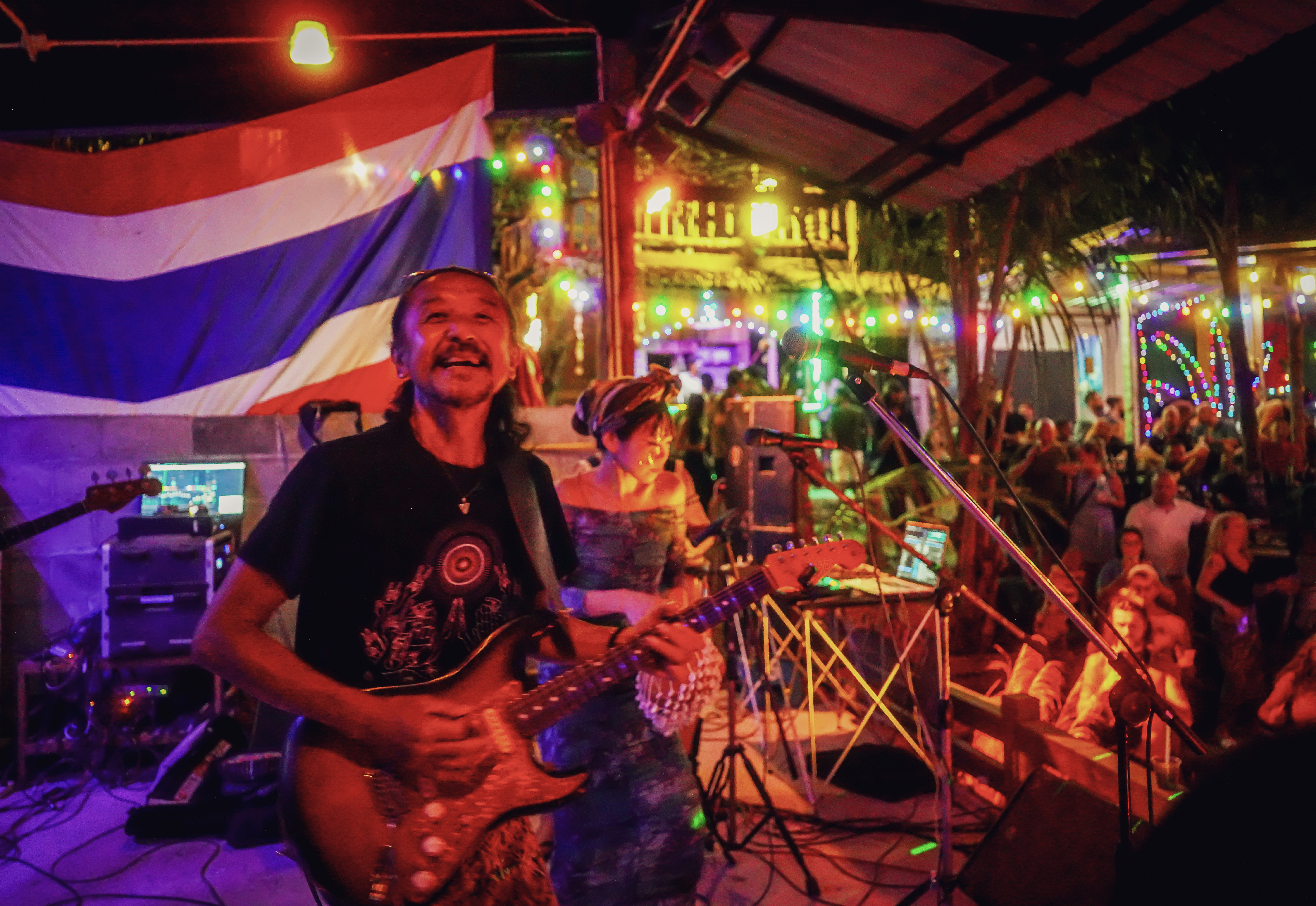 Guitarist and singer performing with thai flag and stage lights.