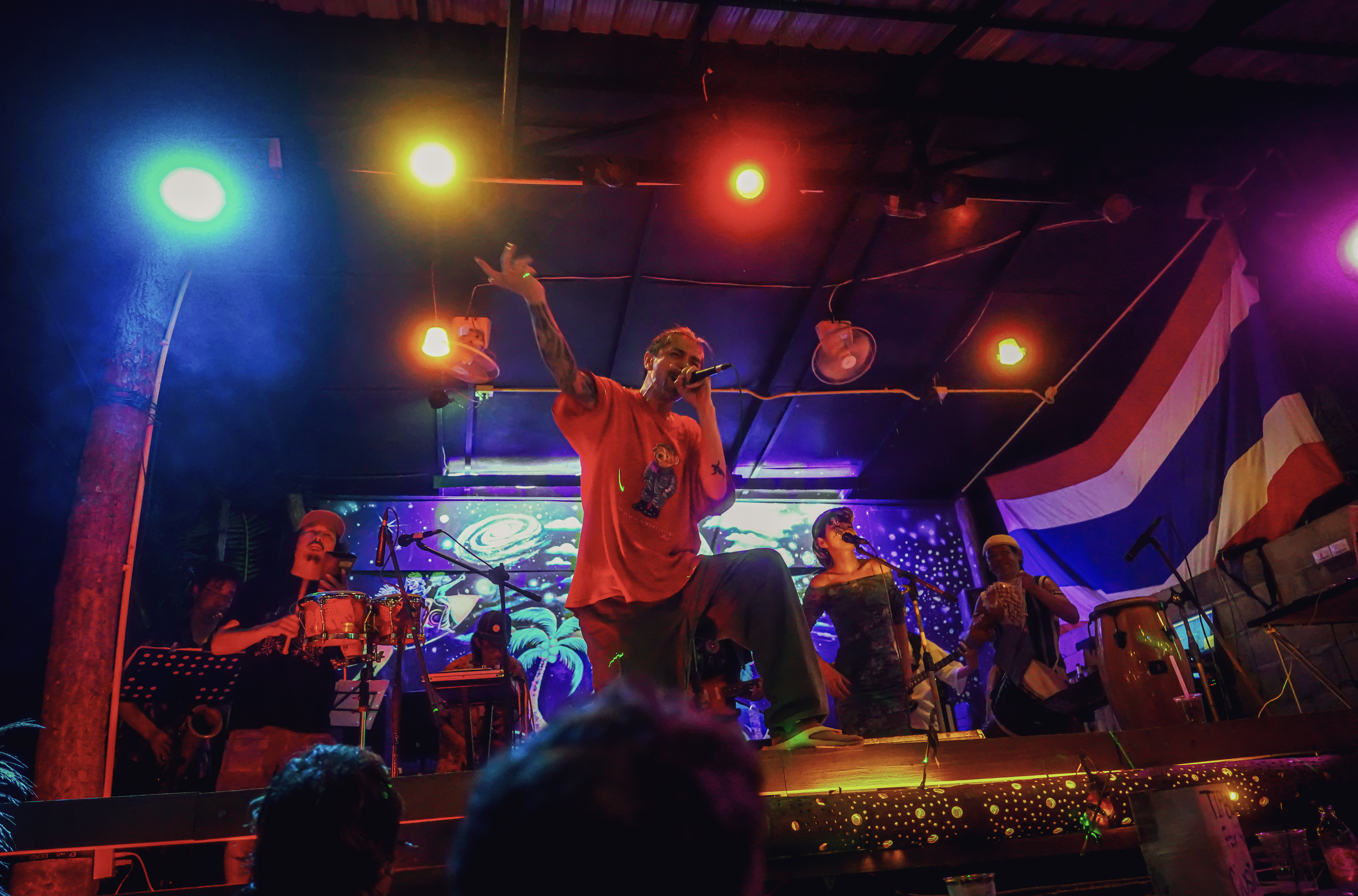 Rap performer on stage with Thai flag and vibrant lights.