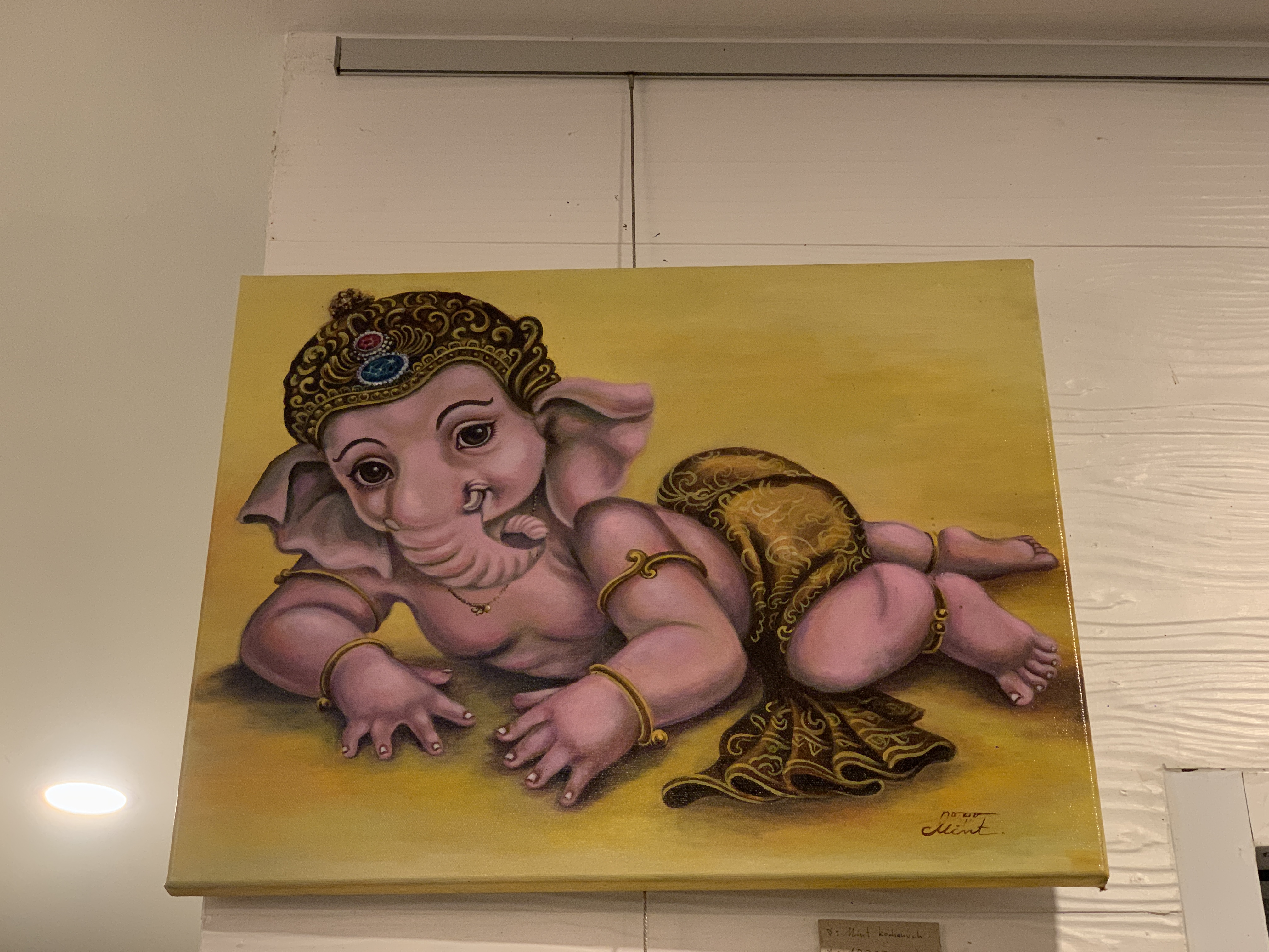 Painting of Baby Ganesha in a playful pose on a yellow background.