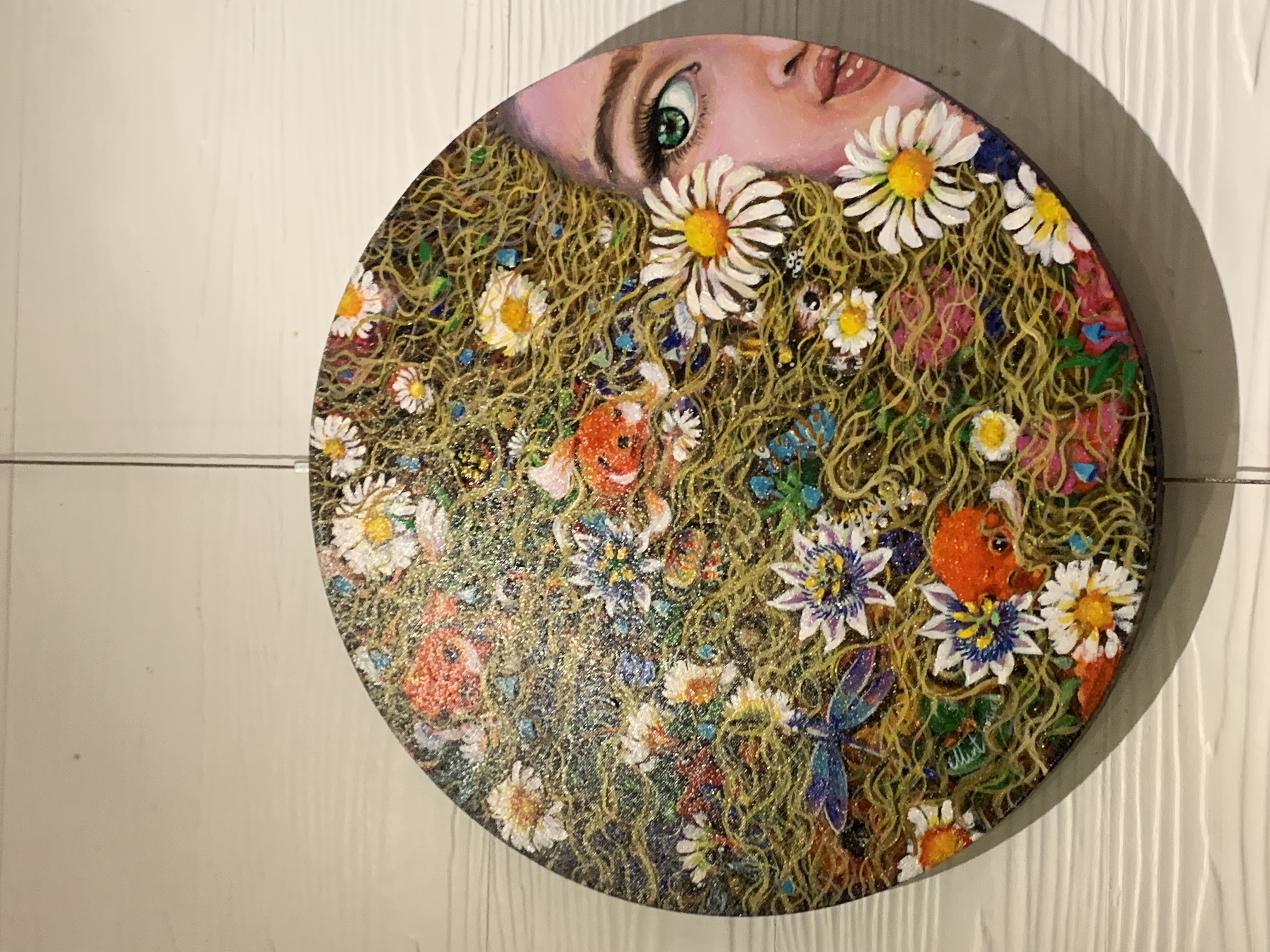 Round painting of a woman's face blending into a field of flowers.