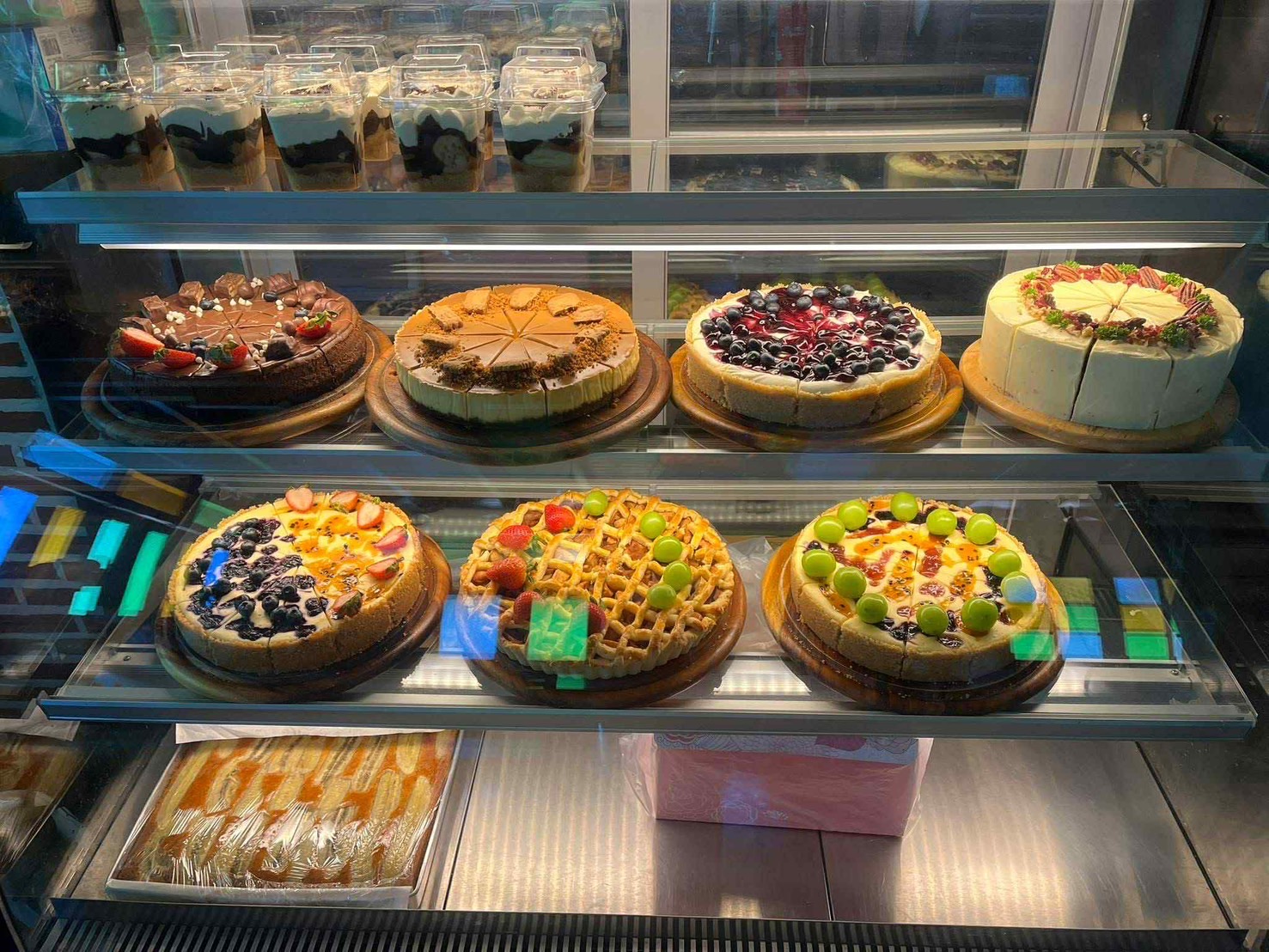 Bakery showcase featuring whole cheesecakes, fruit cakes, and layered dessert cups.